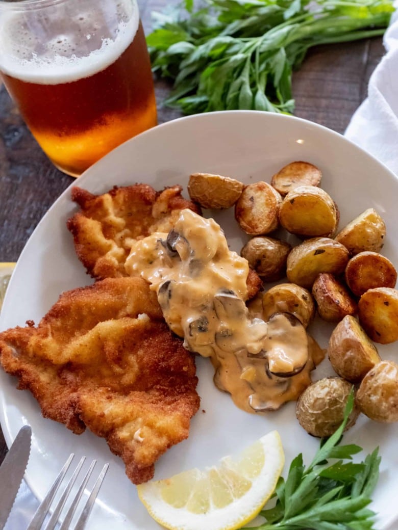 jaegerschnitzel on a plate with potatoes and a glass of lager
