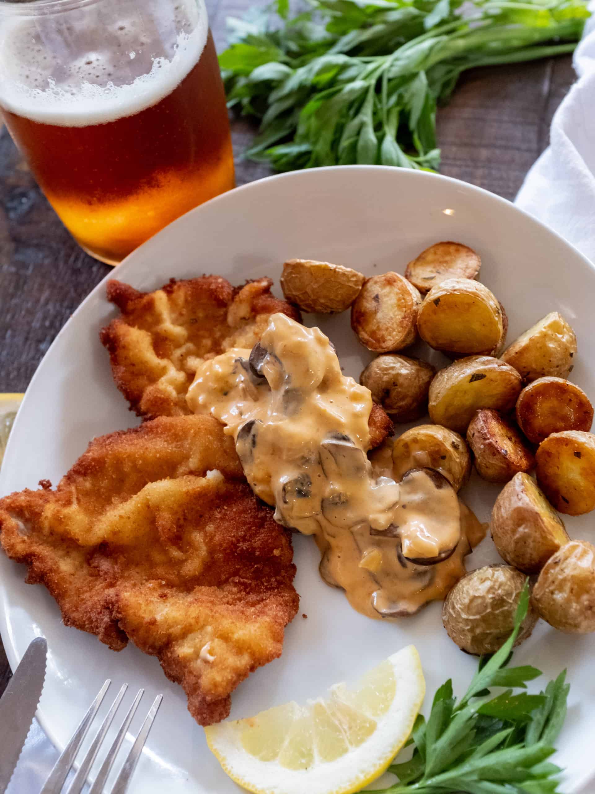 jaegerschnitzel on a plate with potatoes and a glass of lager