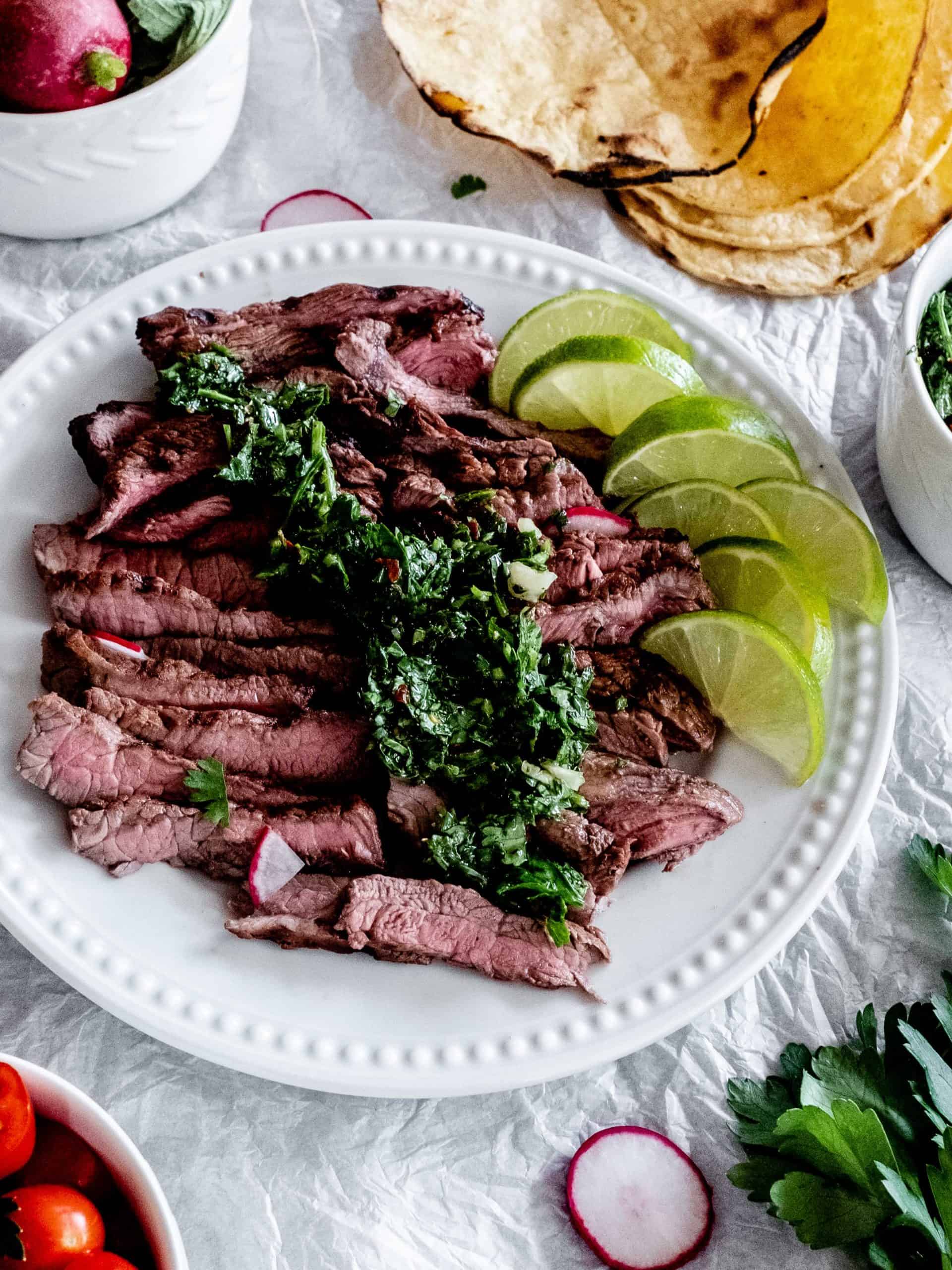 grilled steak with chimichurri and lime wedges