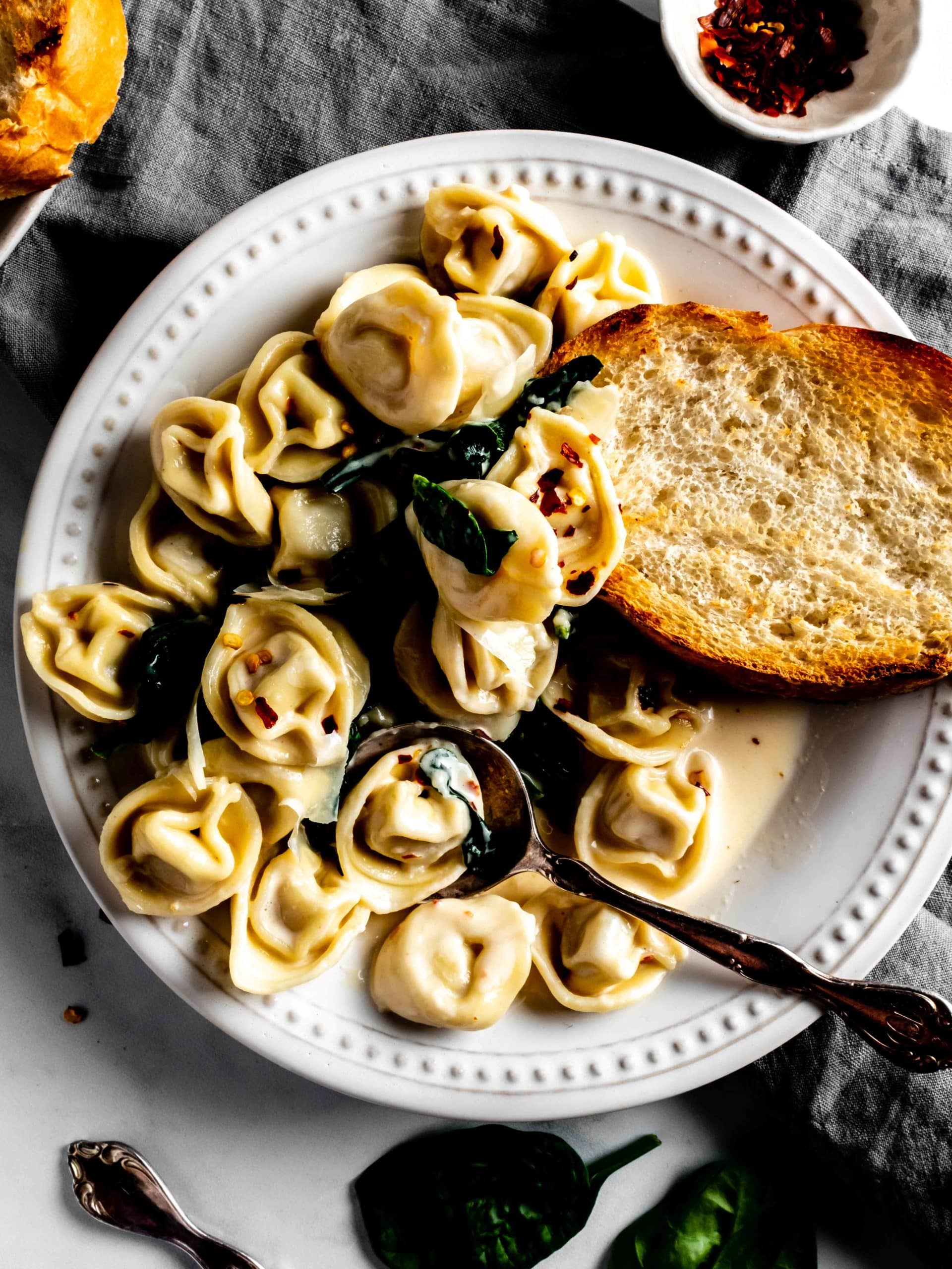 plate of tortellini with white wine cream sauce, toasted bread and spinach