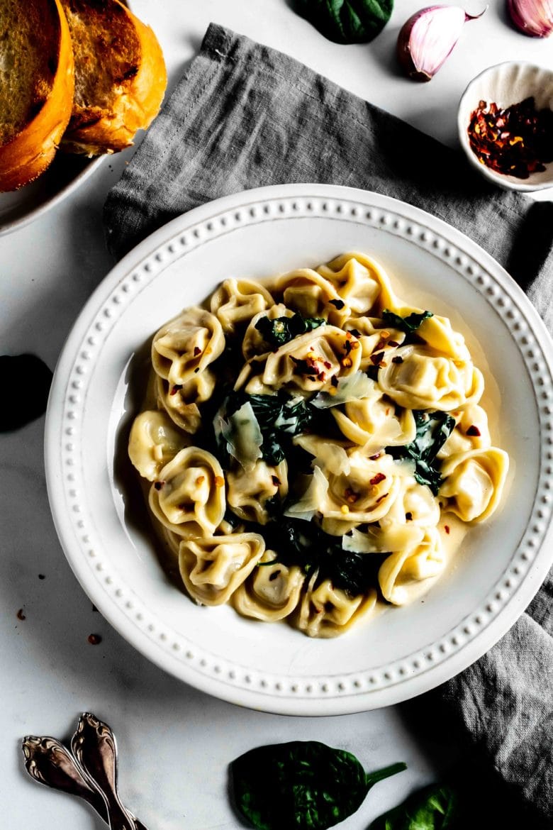 plate of tortellini in cream sauce with spinach and red pepper flakes