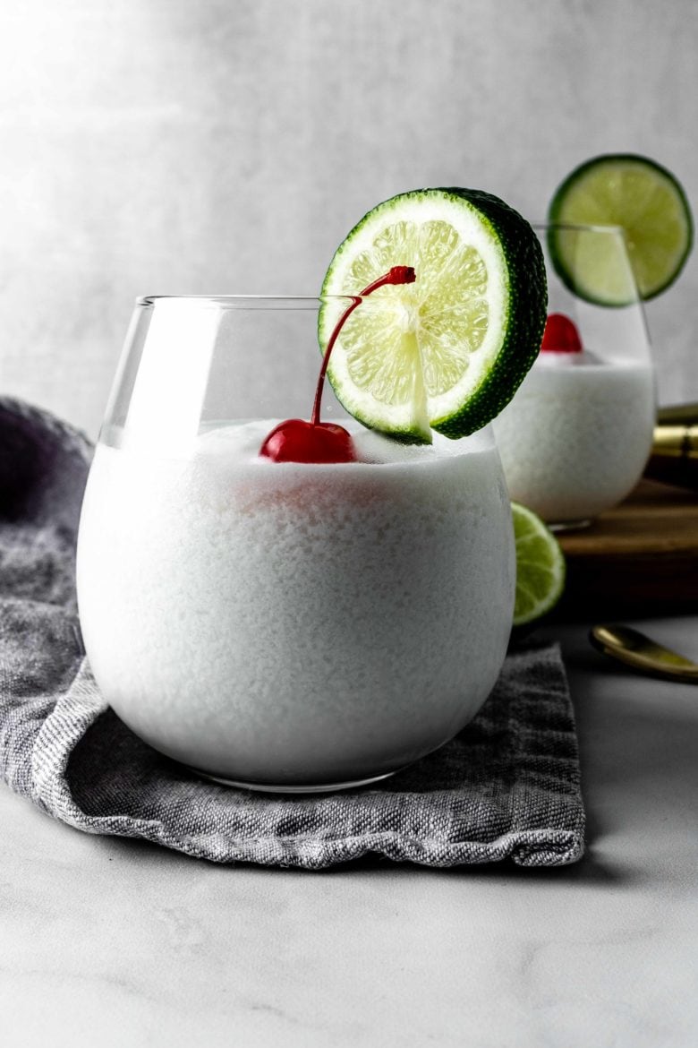 glass of limonada de coco with cherry and lime garnish