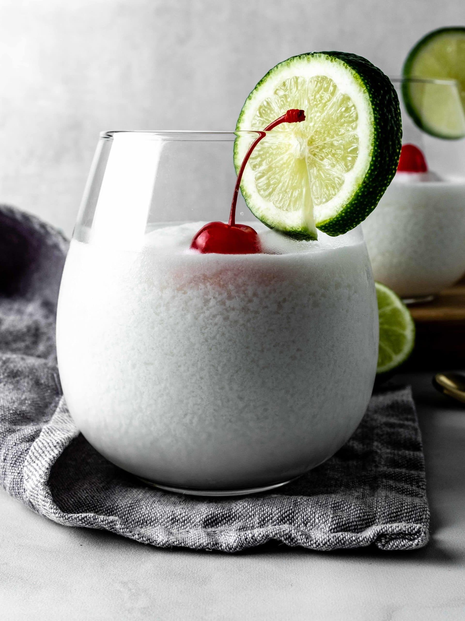 glass of limonada de coco with cherry and lime garnish