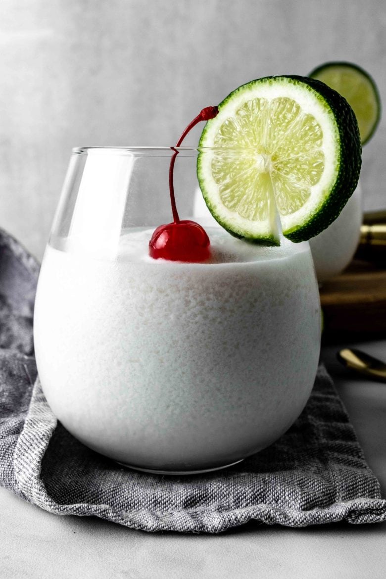 glass of limonada de coco with cherry and lime garnish