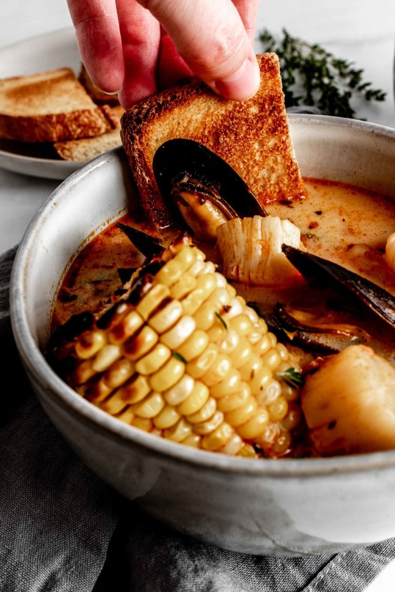 dipping piece of toast into corn and seafood stew