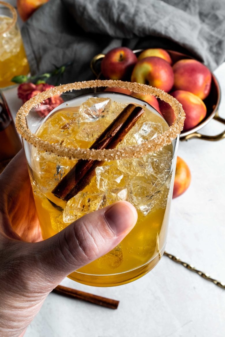 holding a glass of apple cider rum cocktail