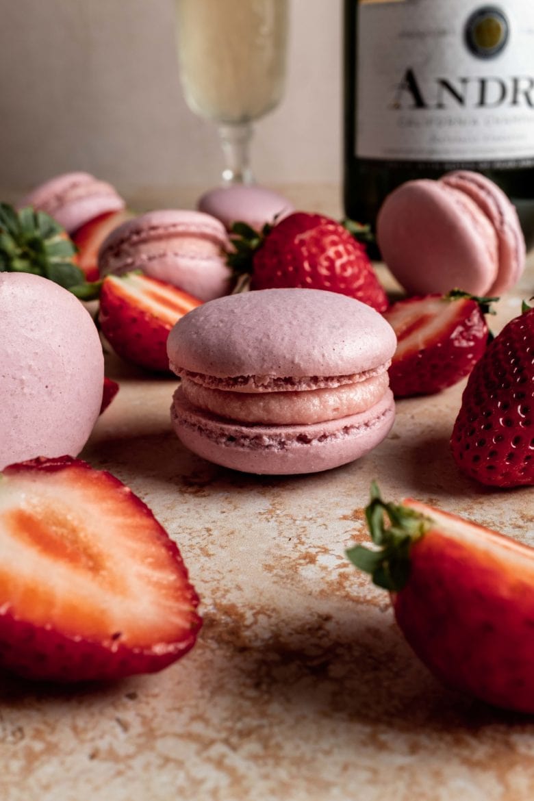 champagne strawberry macaron surrounded by sliced strawberries