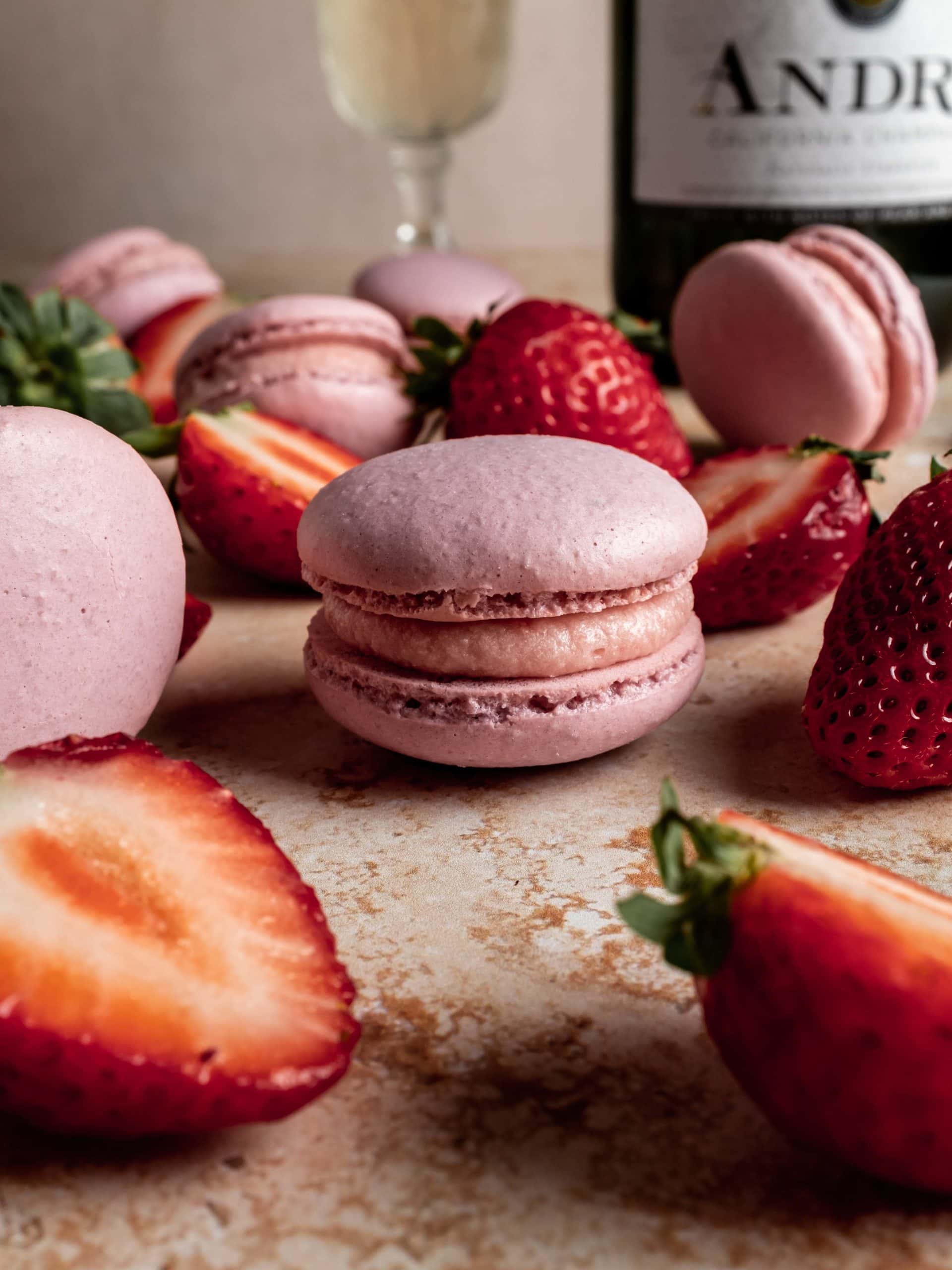 champagne strawberry macaron surrounded by sliced strawberries