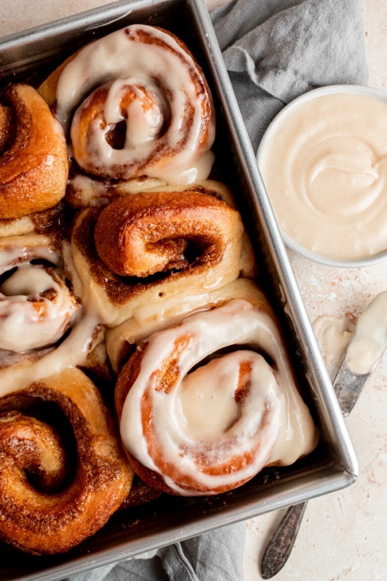 baked cinnamon rolls in pan with bowl of frosting