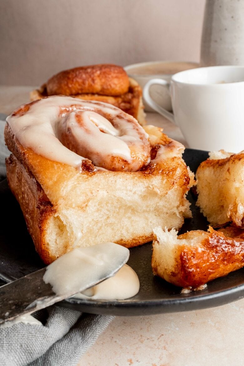 cinnamon roll on plate with frosting and coffee