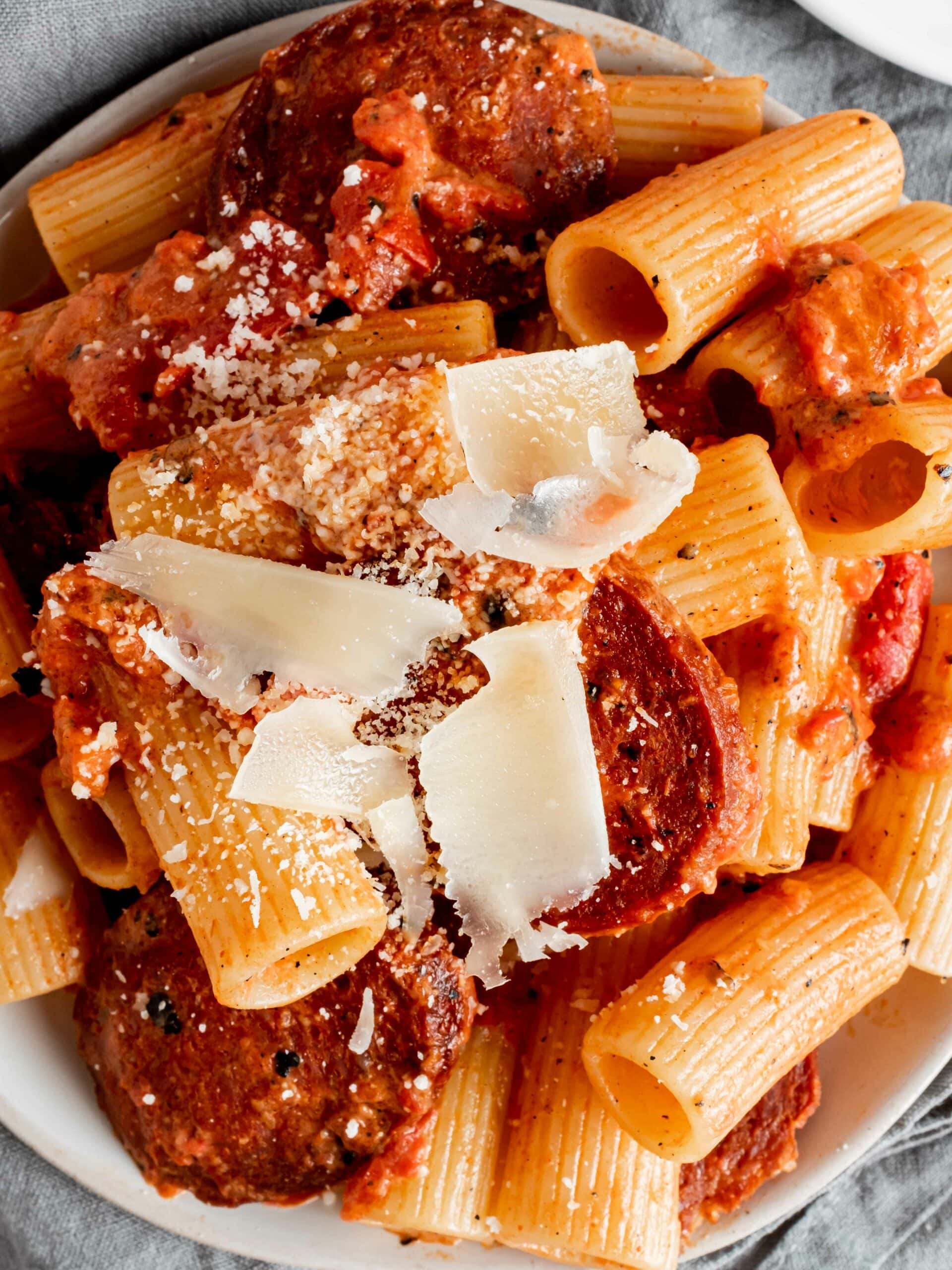 overhead view of pasta on plate with creamy tomato sauce, slices of chorizo and parmesan