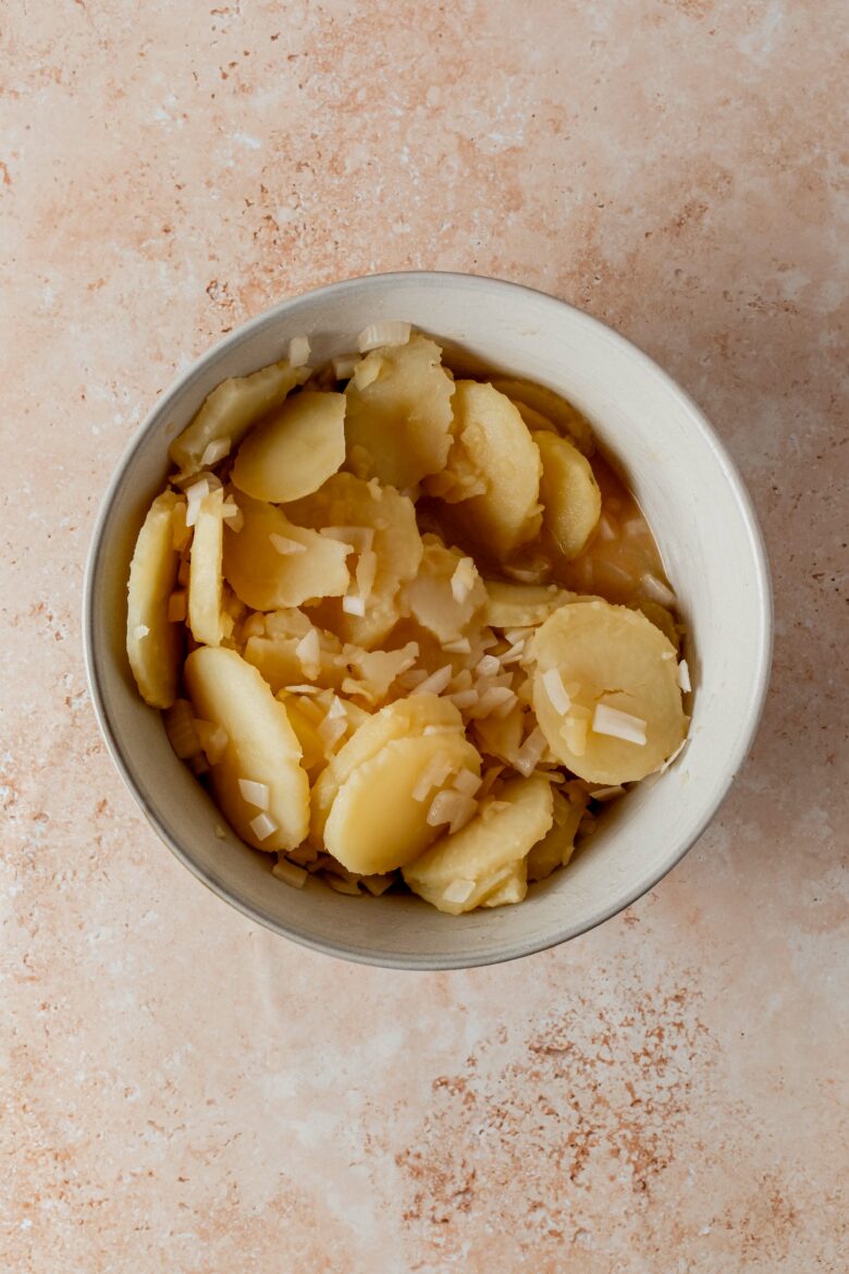 Sliced potatoes marinating in vinegar, broth, mustard and onions.