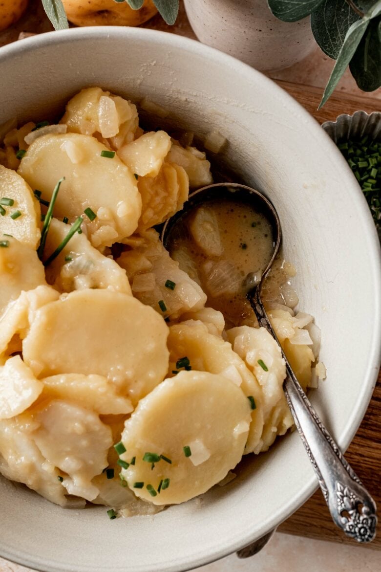 Spoon in bowl of potato salad scooping up vinegar-based dressing.