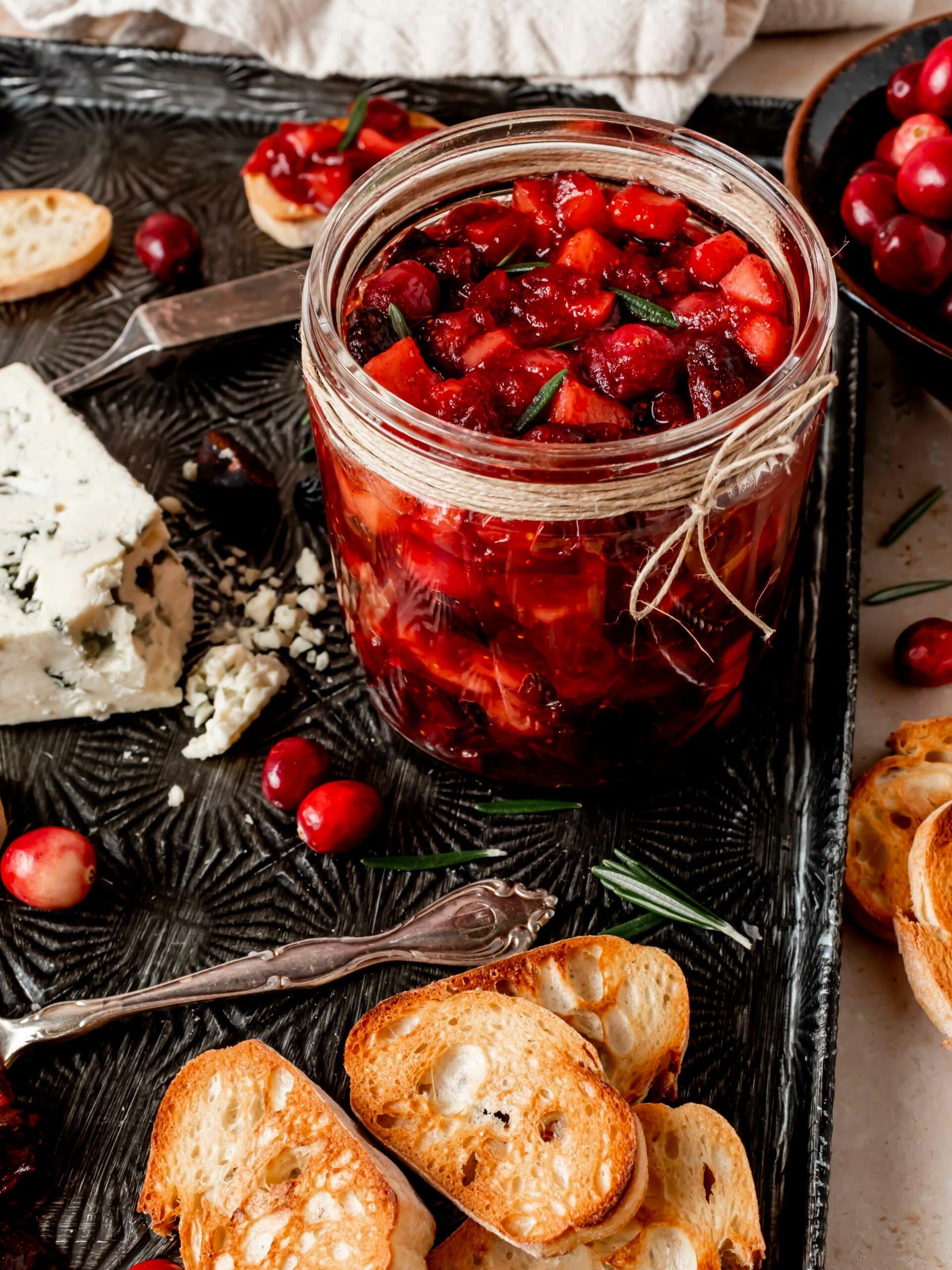 Apple cranberry chutney in a jar on a serving platter with crostini and blue cheese.