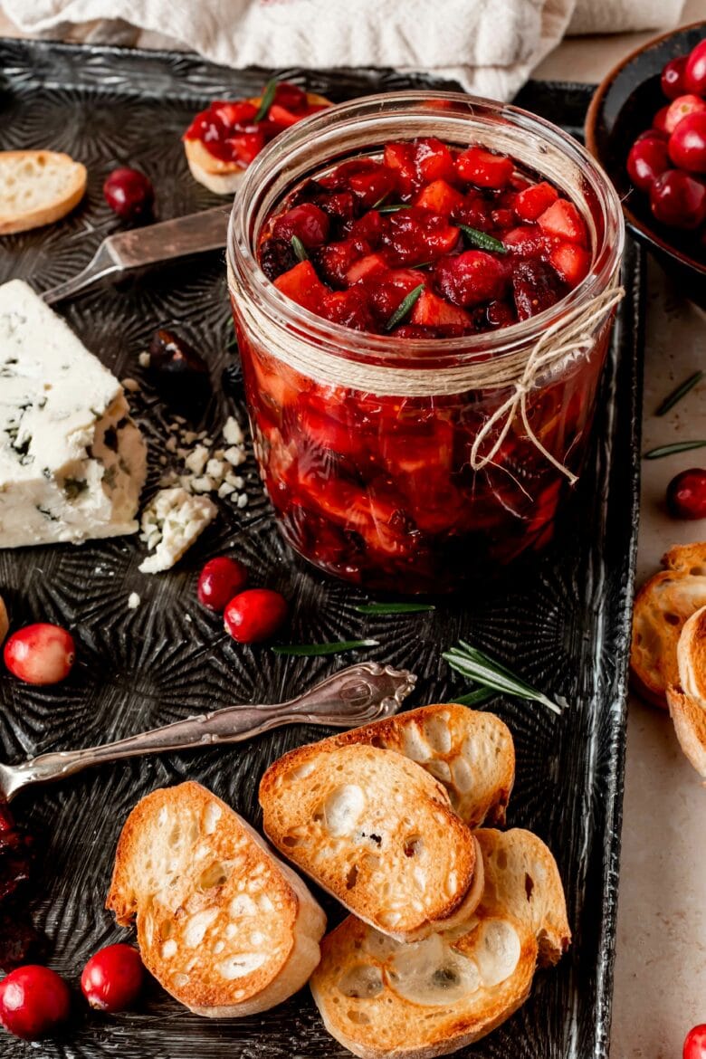 Apple cranberry chutney in a jar on a serving platter with crostini and blue cheese.