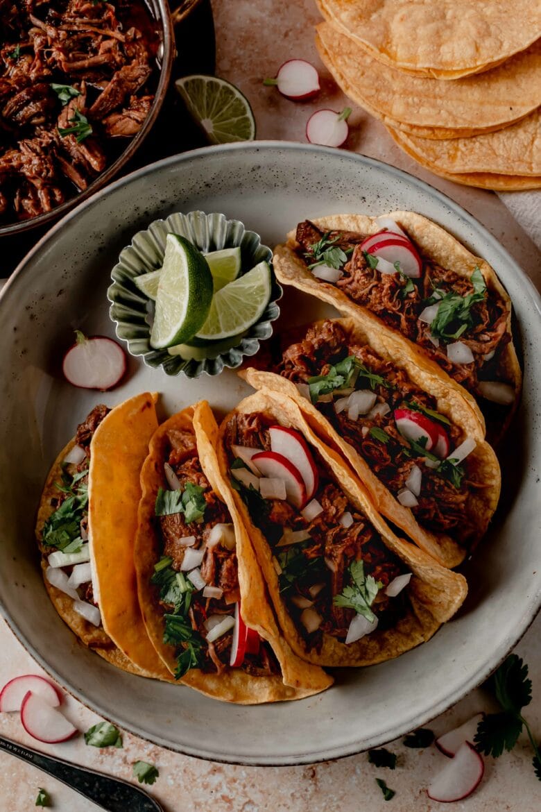 Platter with tacos, toppings and lime slices.