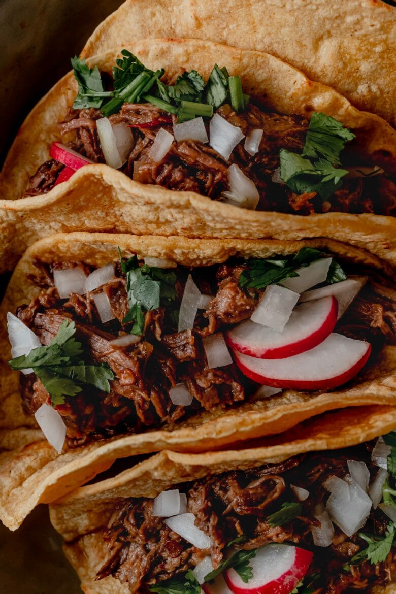 Shredded barbacoa beef in corn taco shells with diced onion, cilantro and radishes.