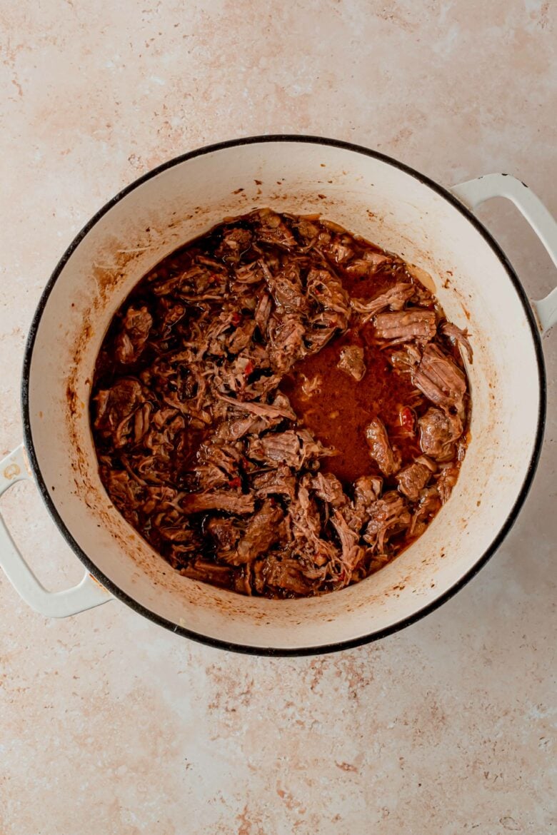 Returning shredded beef to barbacoa sauce in pot.