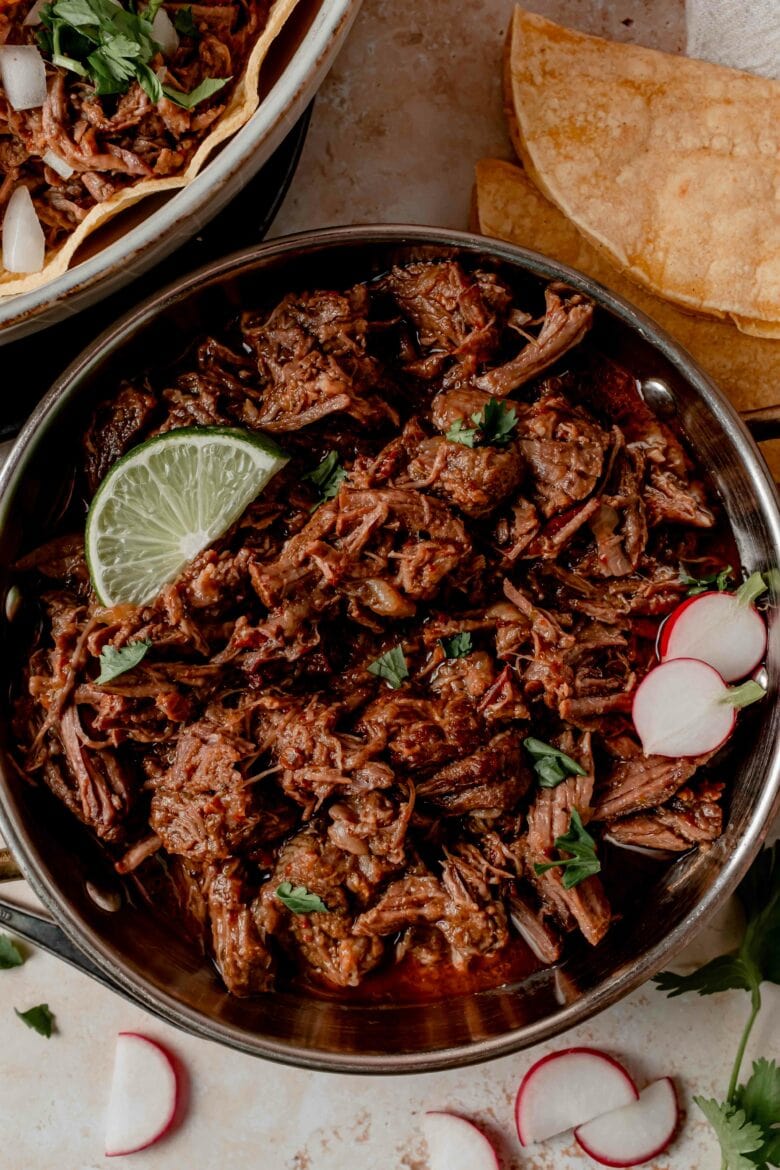 Shredded barbacoa beef on a platter with cilantro, radishes and lime slice.