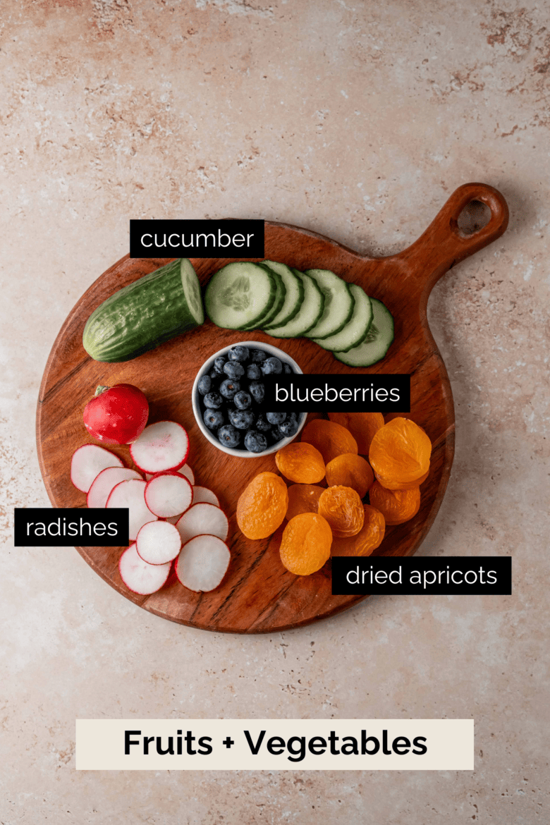 Sliced cucumbers, radishes, blueberries and dried apricots on a cutting board.