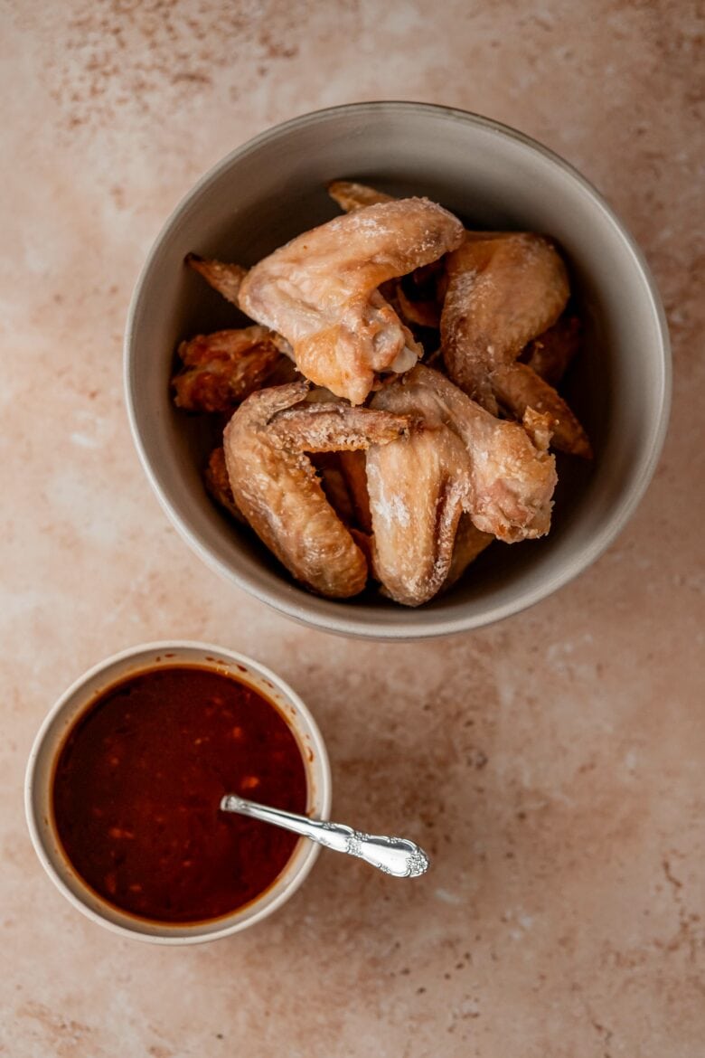 Crispy baked wings in a large mixing bowl alongside a bowl of Gochujang sauce.