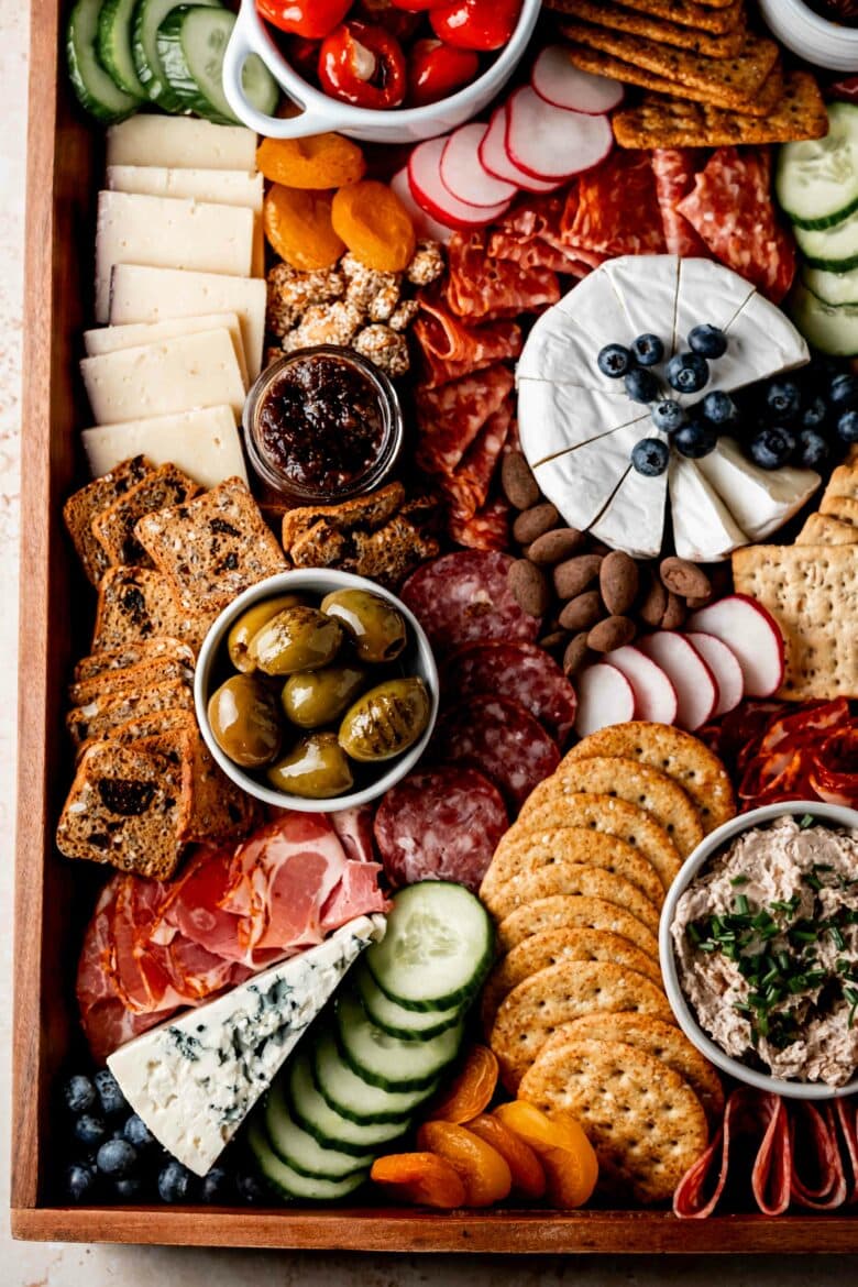 Charcuterie arranged on a serving platter featuring blue cheese, brie, salami, crackers and other small treats.