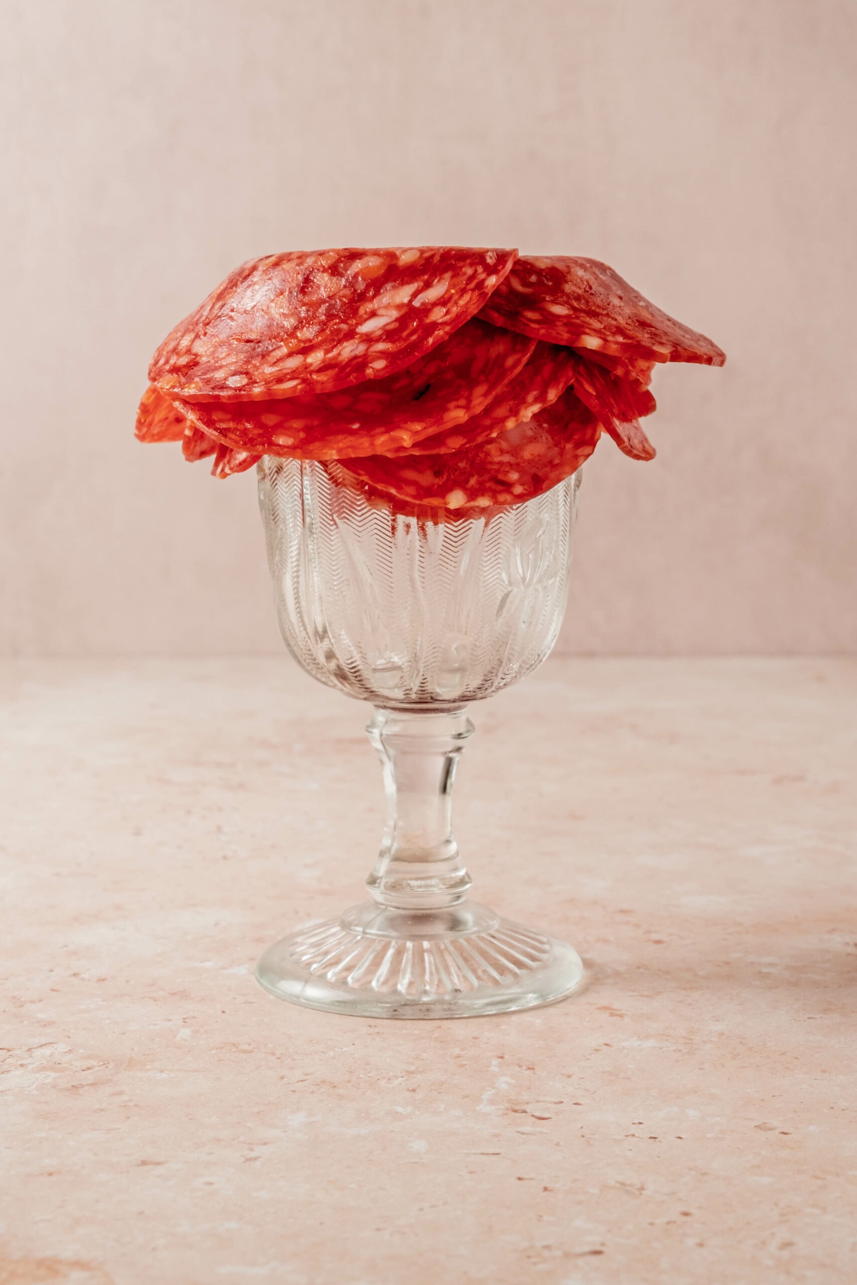 Layering slices of salami on the rim of the glass.