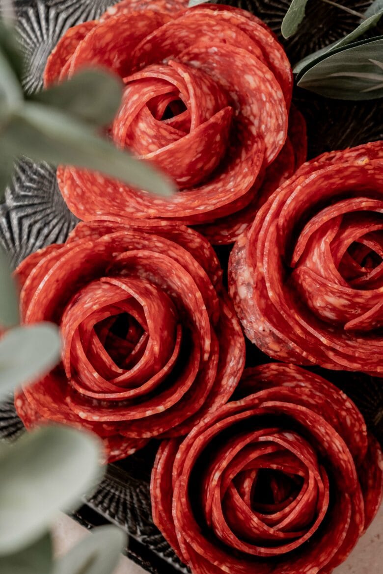 Four salami roses arranged on a metal tray.