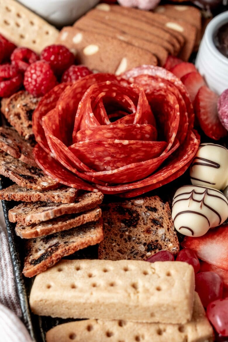 Salami rose arranged on a charcuterie board with other small treats.