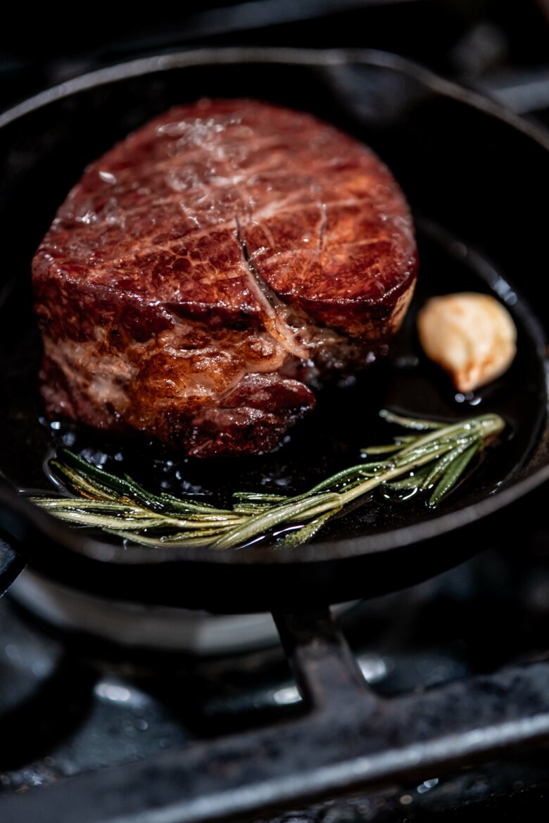 Searing filet mignon in a cast iron skillet with oil, rosemary and garlic.
