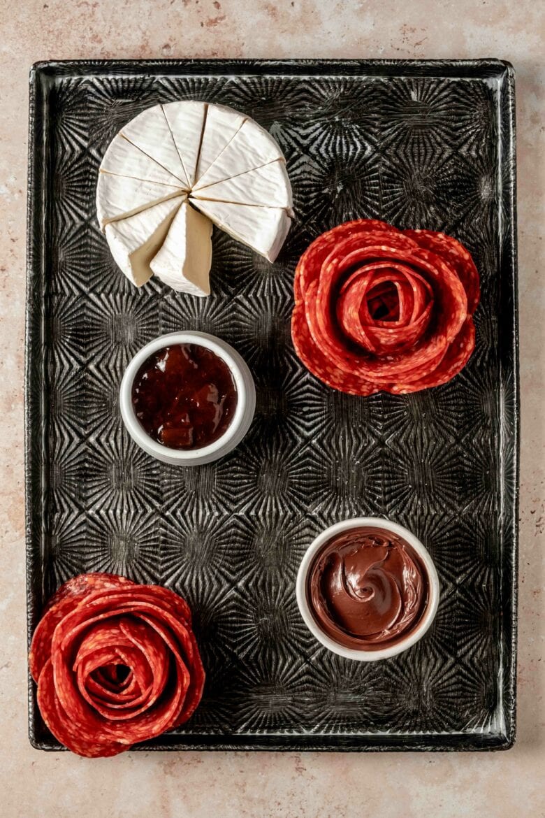 Nutella, jam, salami rose and brie cheese wheel placed on serving tray.