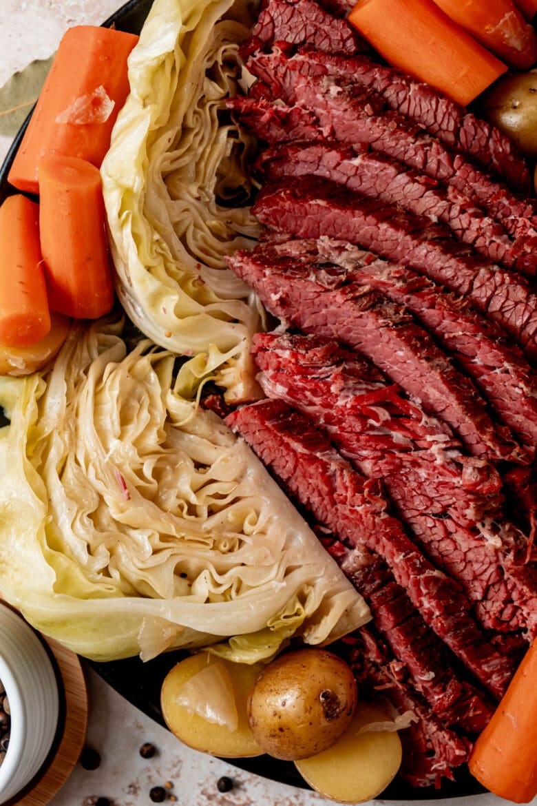 Sliced corned beef on a platter with cabbage, potatoes and carrots.