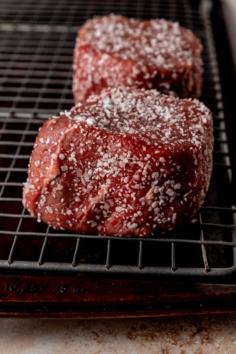 Salted filet mignon steaks on wire rack in rimmed baking sheet.