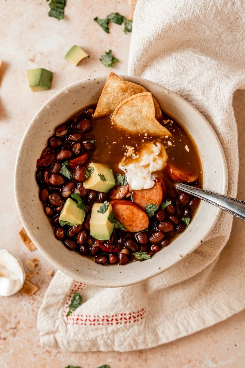 Black bean soup in a bowl garnished with avocado, cilantro, sour cream and tortilla chips.