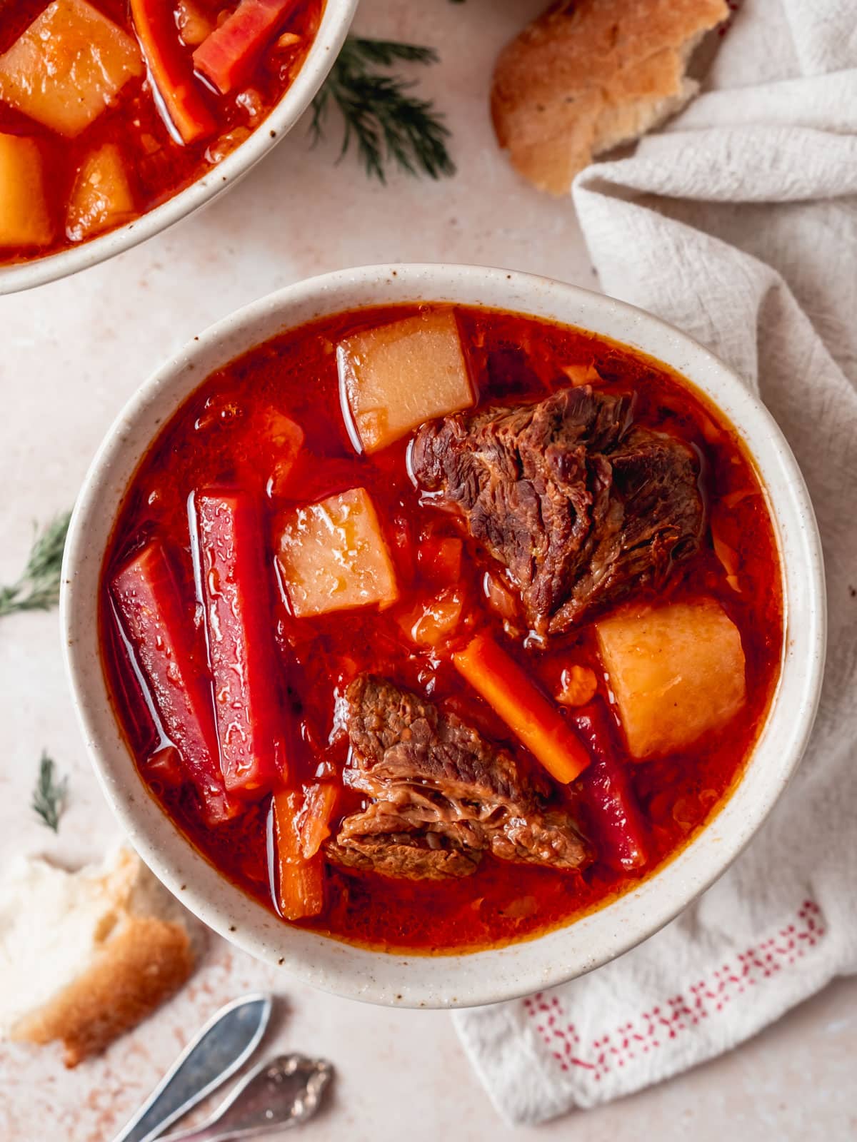 Big bowl of beet borscht with chunks of potatoes and hearty beef pieces.