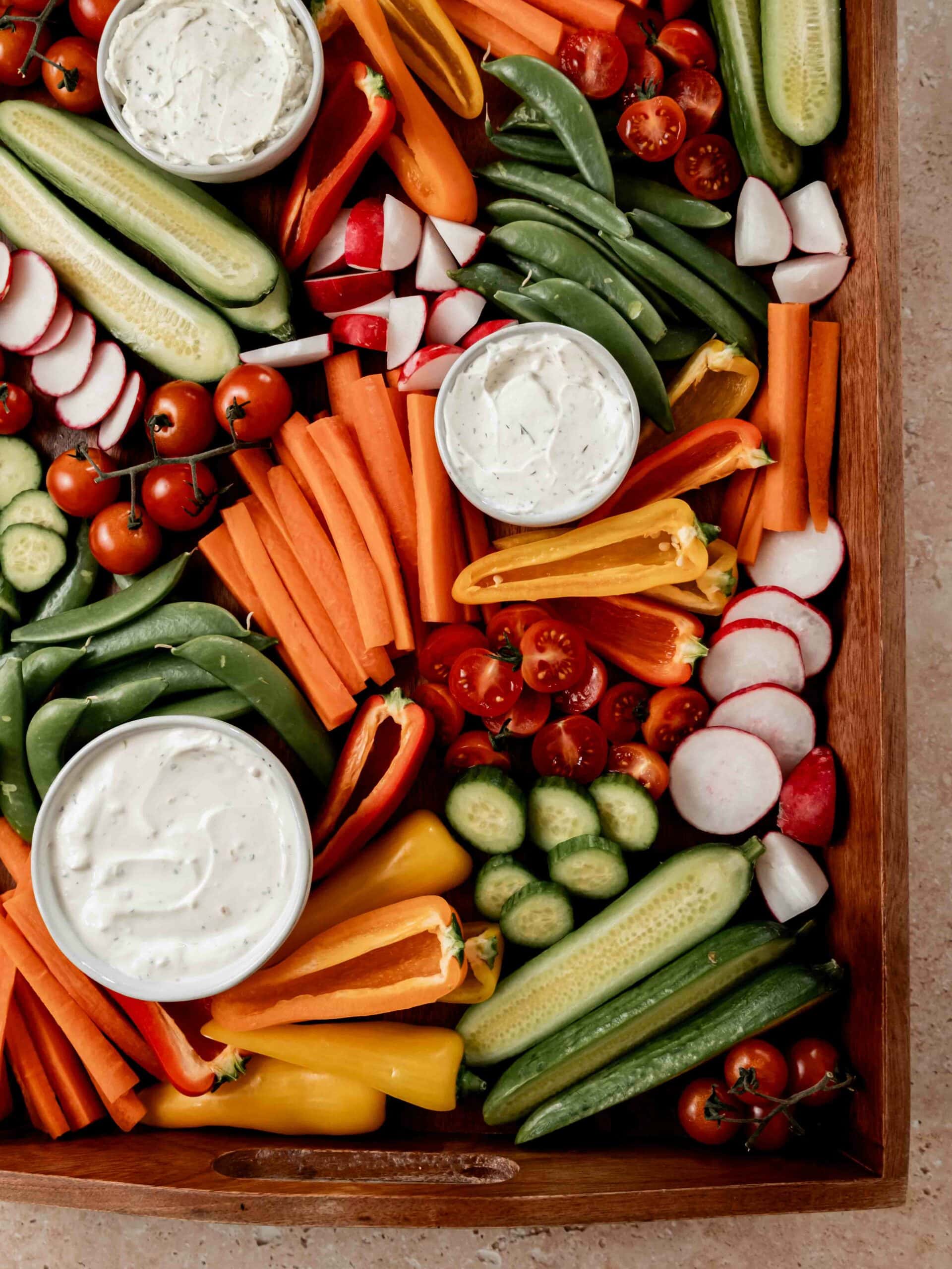 Close up of cut vegetables arranged on wooden serving tray with dips in small bowls.