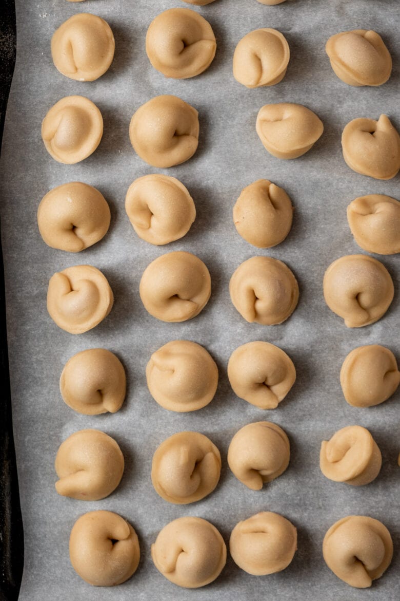Formed pelmeni on a sheet pan lined with parchment paper.