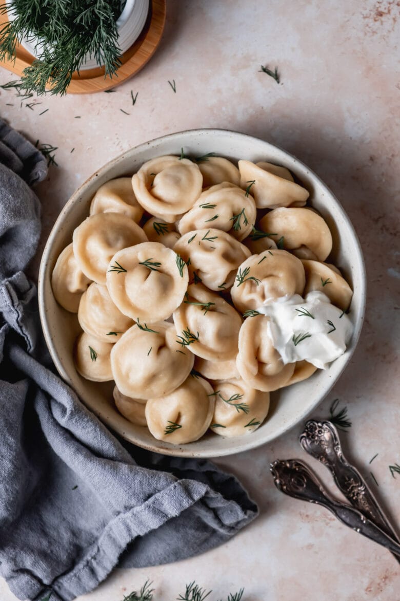 Cooked Pelmeni on a plate with fresh dill and sour cream.