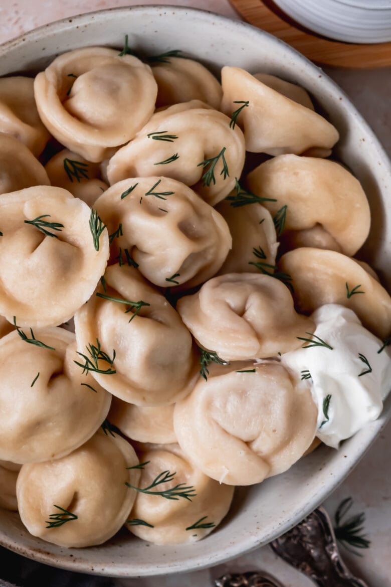 Close up of cooked pelmeni topped with fresh dill.