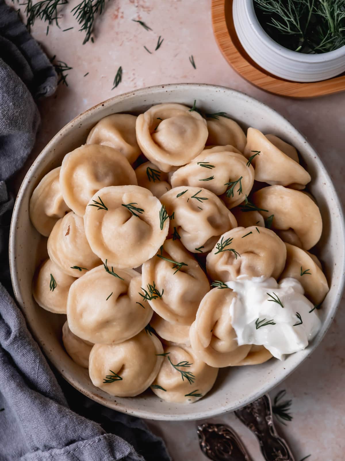 Siberian pelmeni on a plate garnished with fresh dill and sour cream.