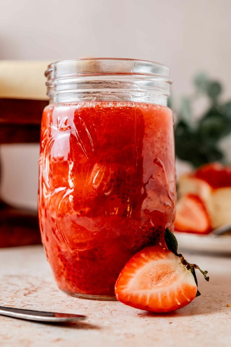 Jar of prepared strawberry sauce with fresh strawberries.