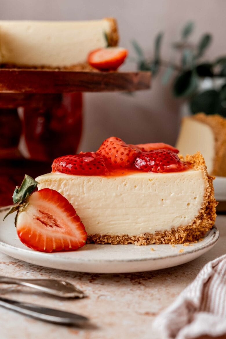 White chocolate cheesecake with graham cracker crust on plate with homemade strawberry topping.