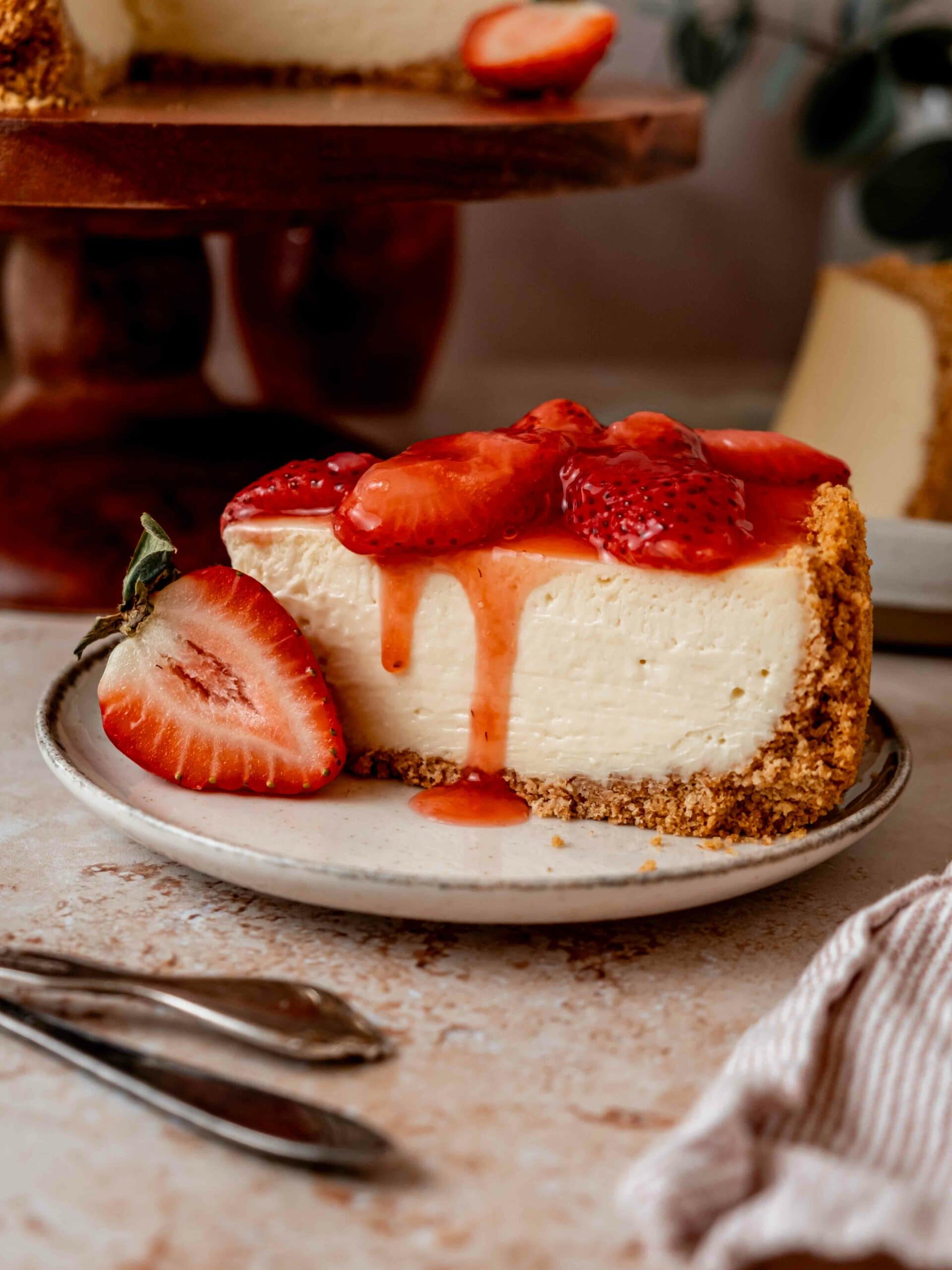 Velvety smooth cheesecake with graham cracker crust on a plate with sweet strawberry topping.