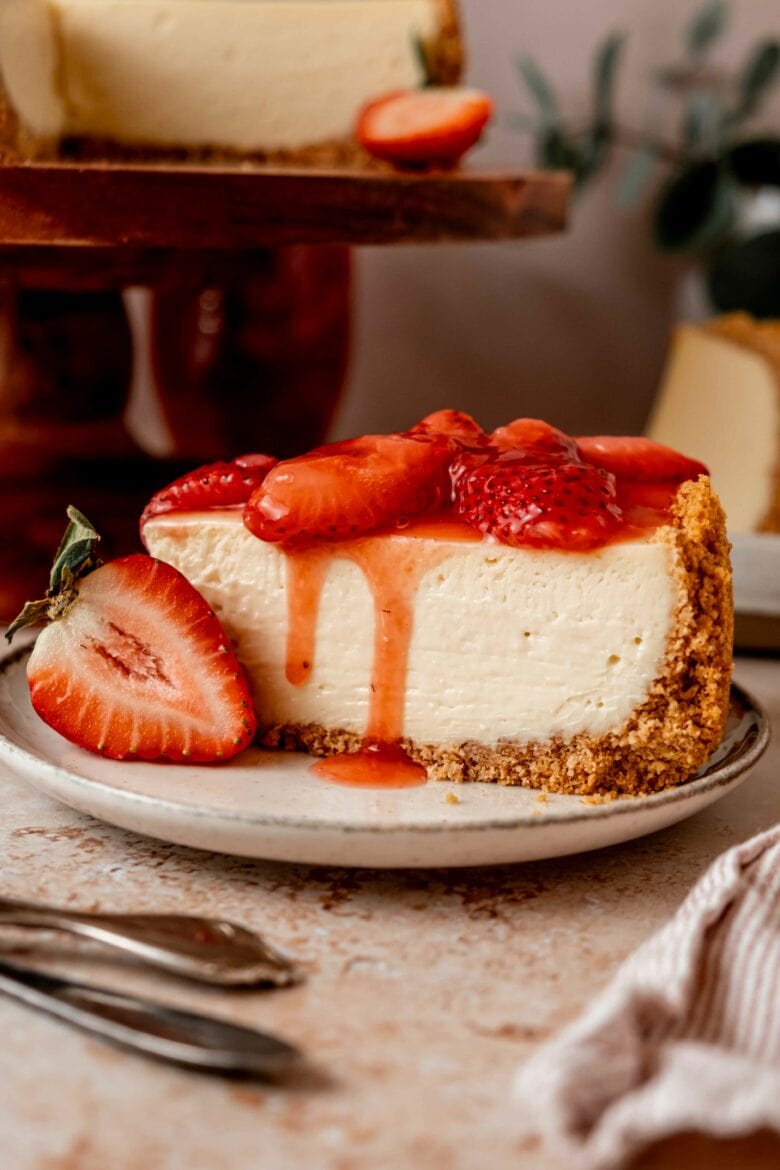 Creamy cheesecake on a plate with strawberry sauce dripping down the sides.