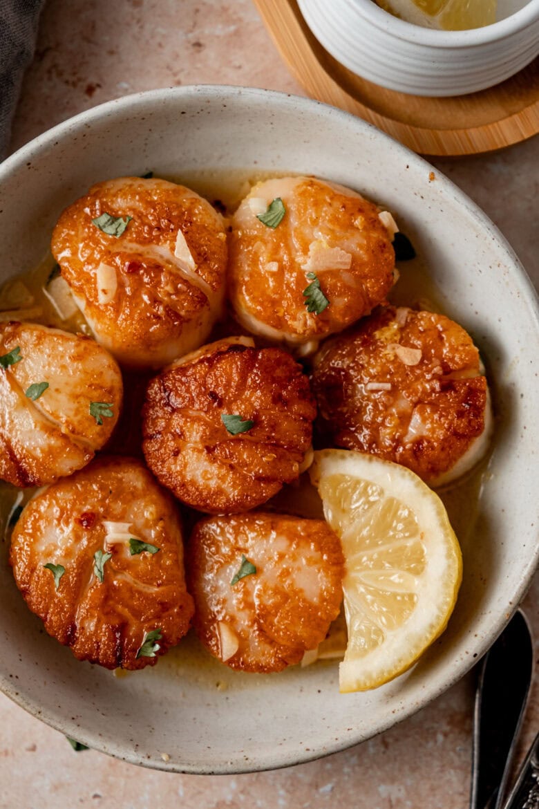 Golden brown seared scallops on a plate with slice of lemon.