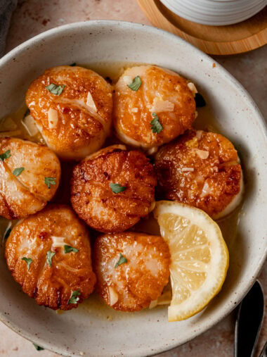 Seared scallops in dish with lemon slice.