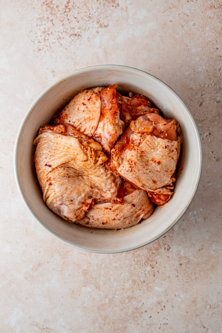 Chicken thighs in a large bowl rubbed with paprika, cayenne and salt.
