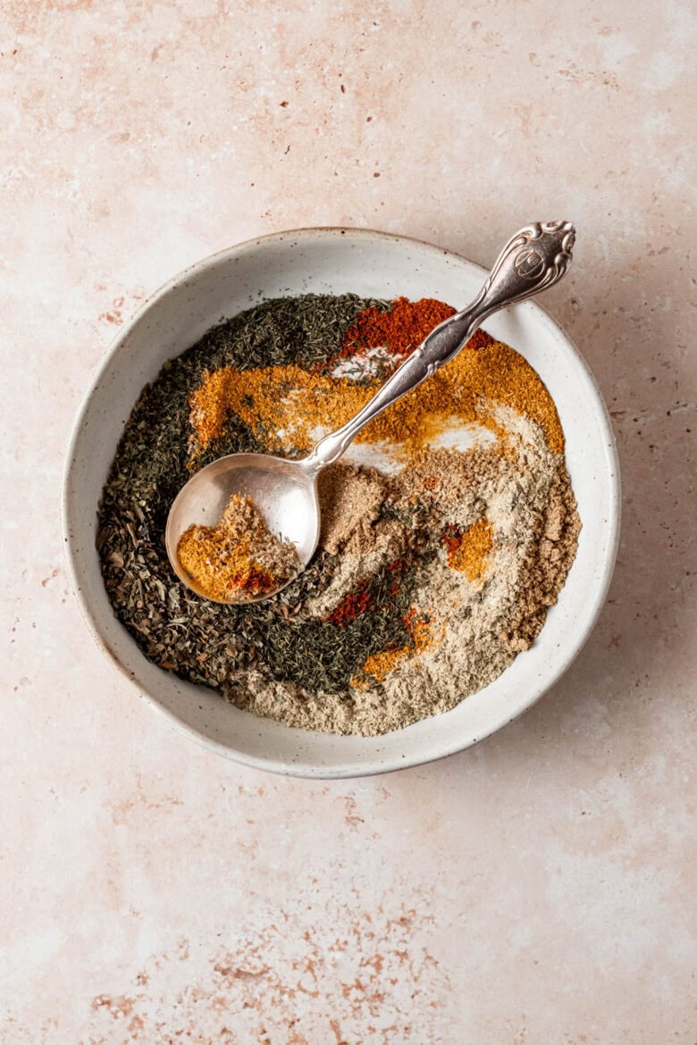 Spoon mixing spices featuring swirls of bright marigold and red cayenne.