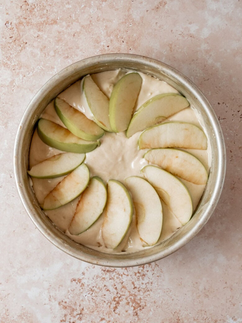 Layering apple slices in circular pattern in cake pan.