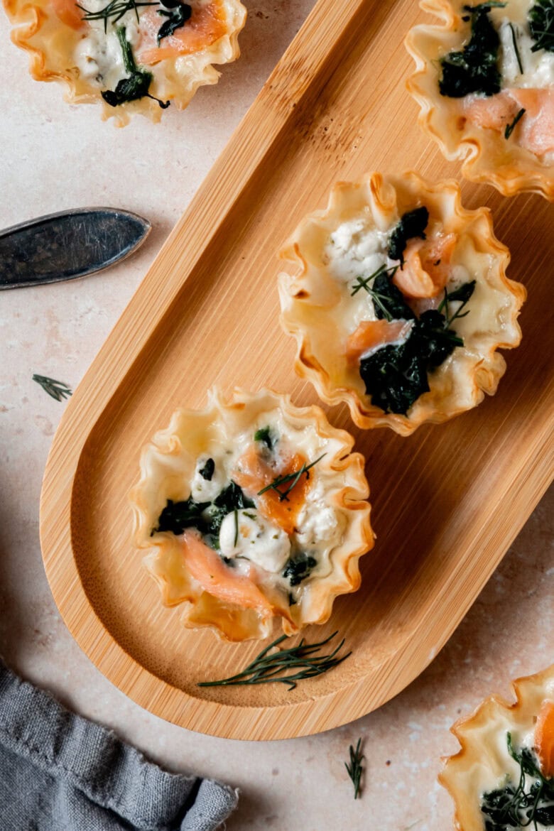 Salmon goat cheese tartlets garnished with dill on small platter.